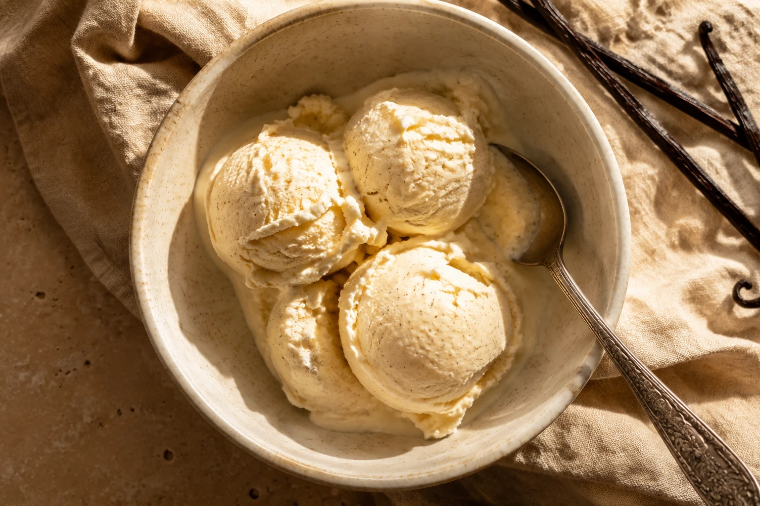 Vanilla bean ice cream in a ceramic bowl with a silver spoon on natural linen